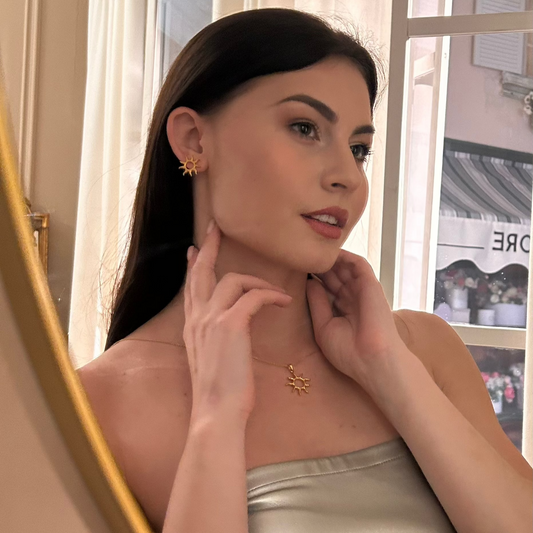 Дівчина дивиться в дзеркало та демонструє срібні сережки і кольє у вигляді сонця від ювелірного бренду Лучі LUCHI